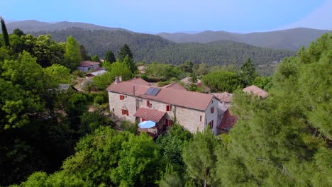 French-villa-in-between-forest-hills-in-the-countryside,-Aerial-dolly-left-reveal-shot