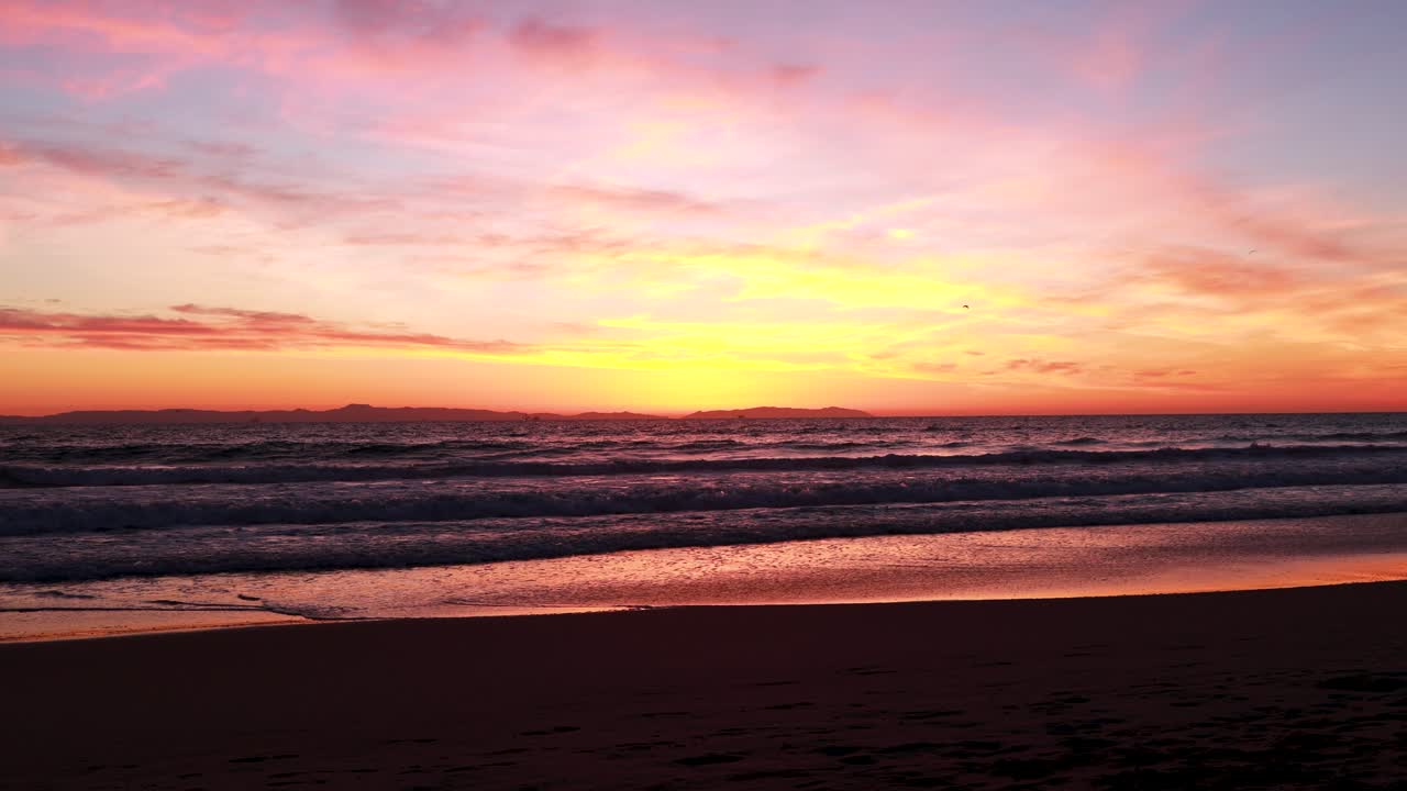 Seagulls fly at the beach during a gorgeous yellow, orange, pink and blue sunset with the Huntington Beach Pier in the background at Surf City USA California