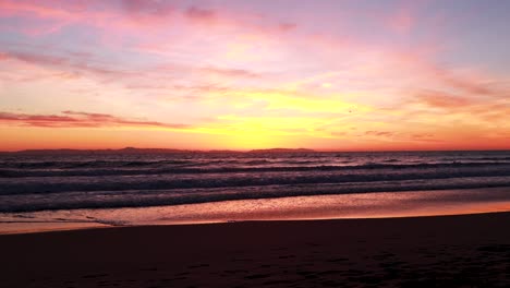 las gaviotas vuelan en la playa durante una hermosa puesta de sol amarilla, naranja, rosa y azul con el muelle de la playa de huntington al fondo en surf city usa california