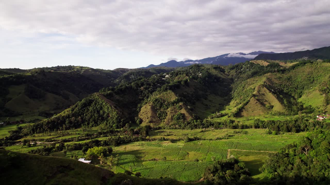 Drone moves forward across patchwork farms in a green Andean valley, Aerial
