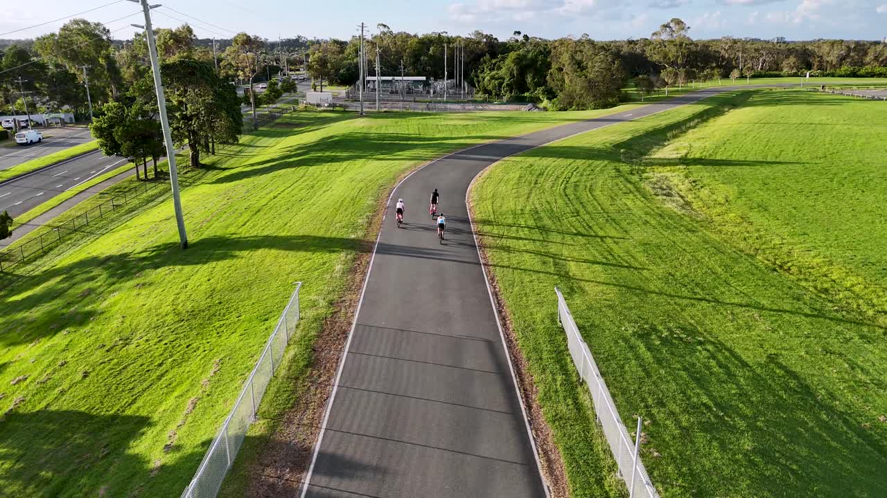 Aerial view of cyclists riding on a winding track surrounded by lush greenery, captured during golden hour lighting