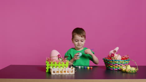 little cheerful boy crafting handmade easter decorations by painting