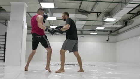 two men in a white gym. the coach and the fighter work out the kick in the jump knee on the paws in slow motion