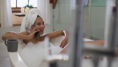 mujer de raza mixta tomando un baño y hablando en el teléfono inteligente