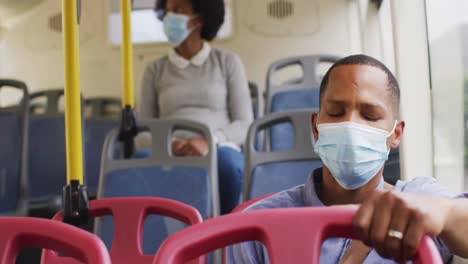 hombre y mujer afroamericanos con máscaras faciales sentados en el autobús