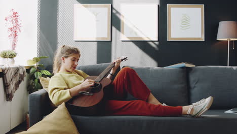 mujer tocando la guitarra en el sofá en la sala de estar