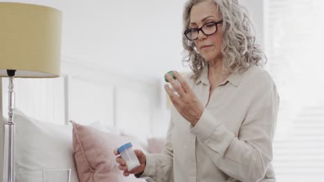 Mujer-Caucásica-Mayor-Con-Gafas-Sentada-En-La-Cama-Y-Leyendo-Botellas-De-Medicina,-Cámara-Lenta