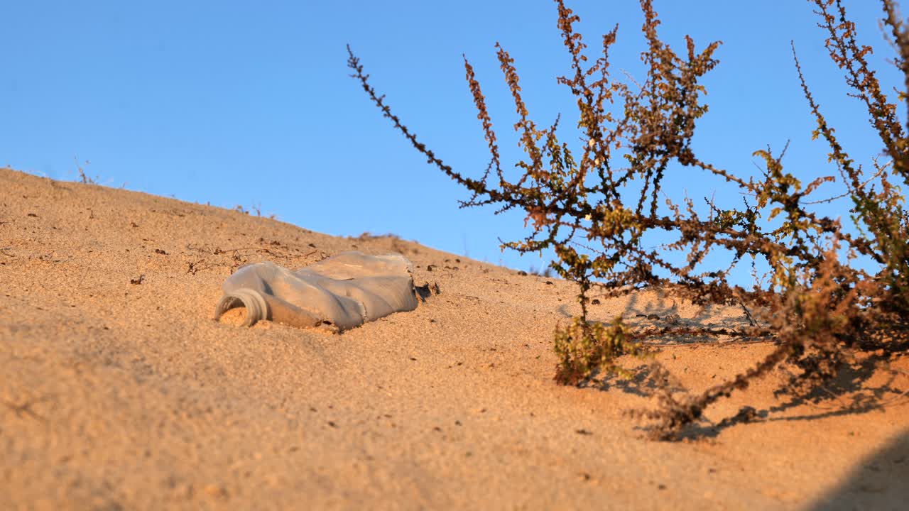 Plastic bottle in sand with desert grass on a Sid 4K