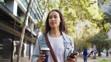 asian woman walking using smartphone and drinking takeaway coffee