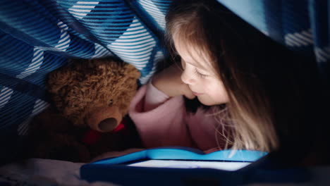 Niña-Feliz-Usando-Una-Tableta-Digital-Bajo-Una-Manta-Disfrutando-Aprendiendo-En-La-Tecnología-De-Pantalla-Táctil-Jugando-Juegos-Divirtiéndose-A-La-Hora-De-Dormir