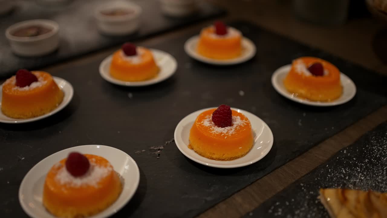 small orange cakes topped with raspberries and coconut flakes on white plates
