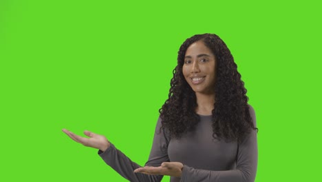 portrait of woman presenting or demonstrating item against green screen smiling at camera