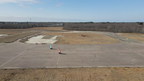 Aerial-footage-of-fly-over-disused-airfield,-chasing-and-tracking-two-Land-Sailing-buggies