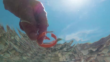 hand pick plastic piece from crystal sea water, underwater shot, look up