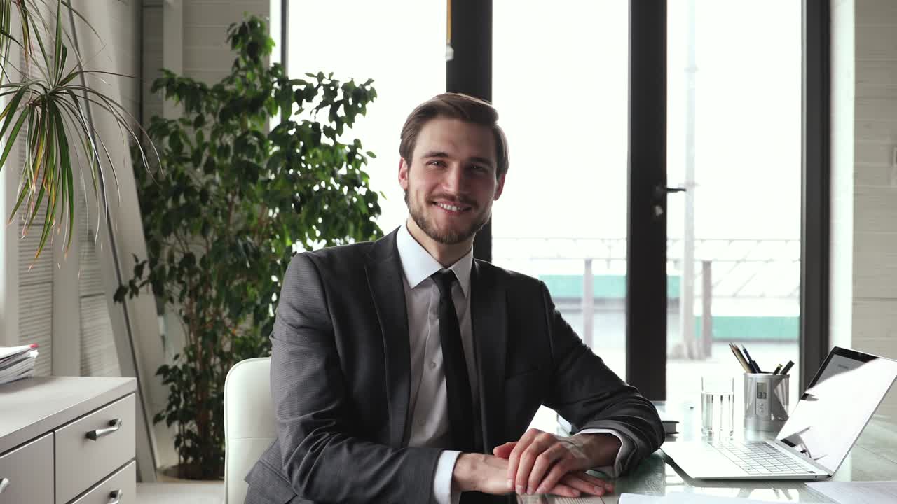 bell'uomo d'affari sorridente che indossa un abito e guarda la telecamera sul posto di lavoro