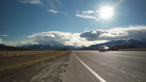 wide angle of vehicles driving down highway with beautiful mountains and clouds in the background as the sun shines overhead