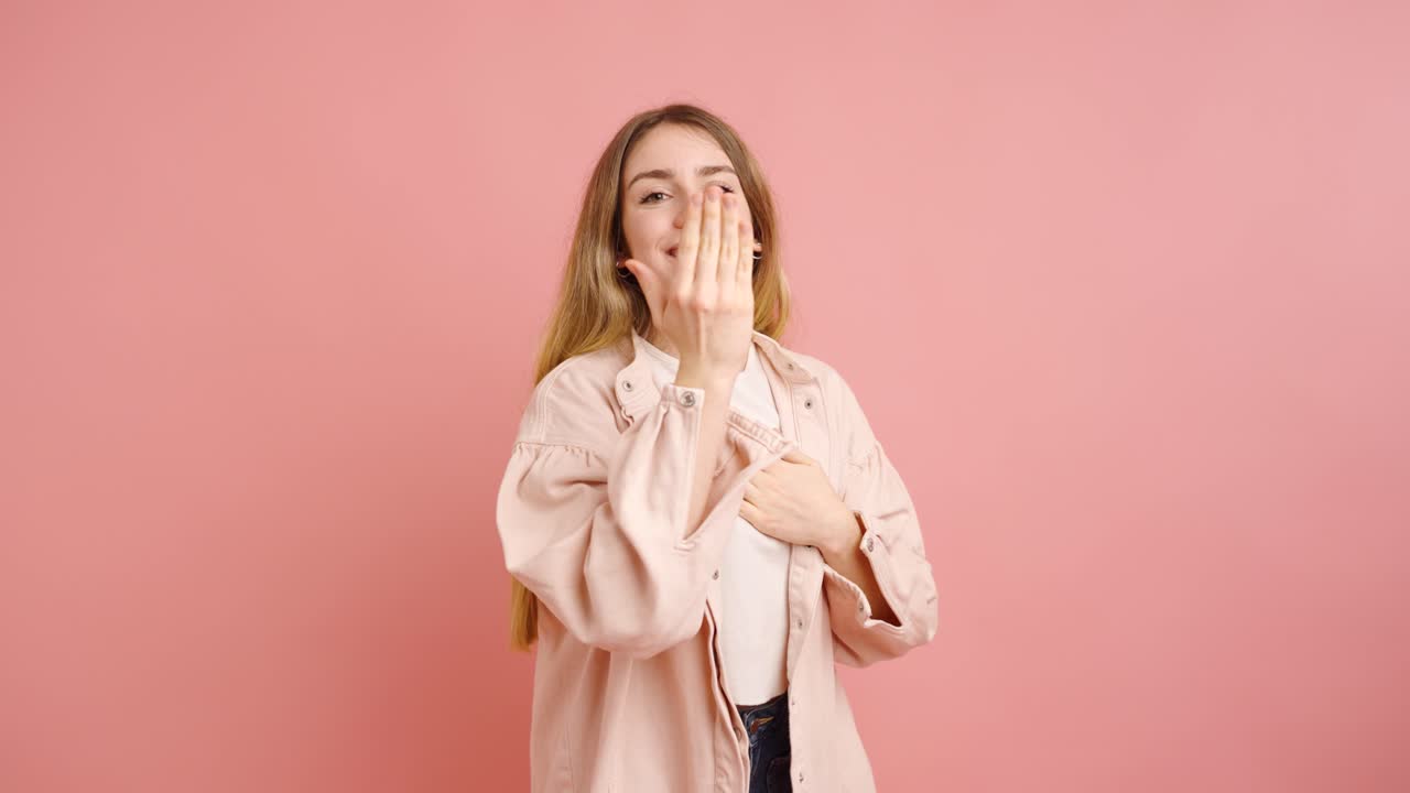 Young woman showing heart sign and blowing kisses on pink background