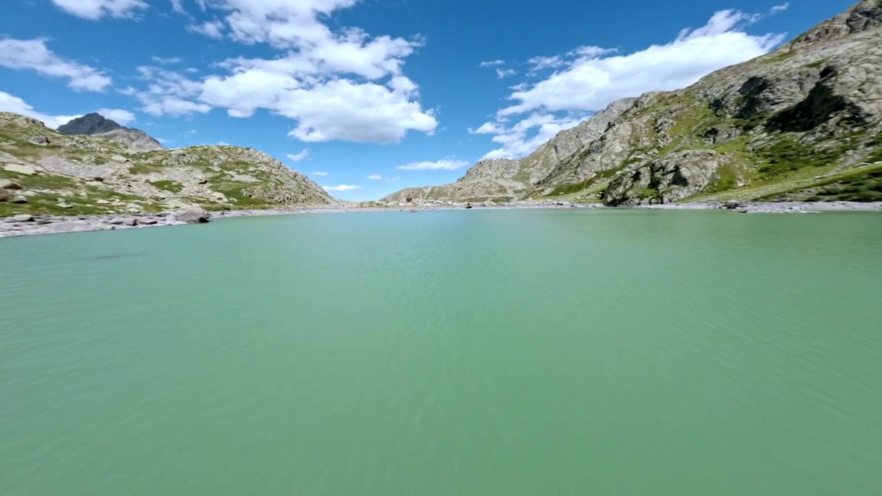 FPV-quadcopter suser lavt over den klippefyldte kystlinje og det turkise Chiotas-reservoir, hvilket skaber en hurtig, fordybende flyvning over alpint vand