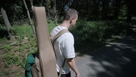 young man walking with guitar on street near forest