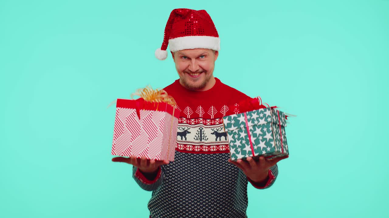 빨간색 새해 옷을 입은 남자가 크리스마스 선물 상자를 선물하고, 카메라에 손을 고 웃는다.