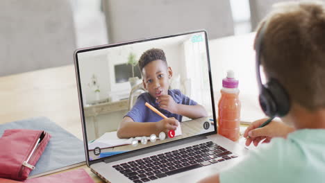 caucasian boy using laptop for video call with african american school friend on screen