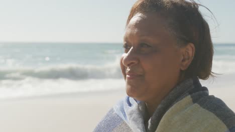 smiling senior african american woman with blanket on sunny beach