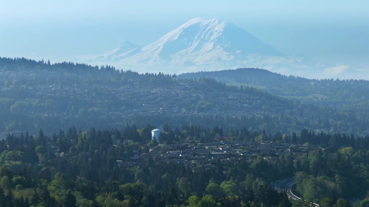 Güneşli bir yaz öğleden sonrası, berrak mavi gökyüzü altında, arka planda devasa karla kaplı Rainier Dağı ile yemyeşil orman ve Bellevue Washington banliyö bölgesi. Geniş sinematik hava çekimi.