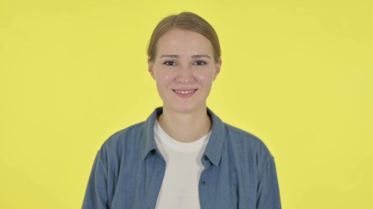 mujer joven mostrando el signo de la victoria en fondo amarillo