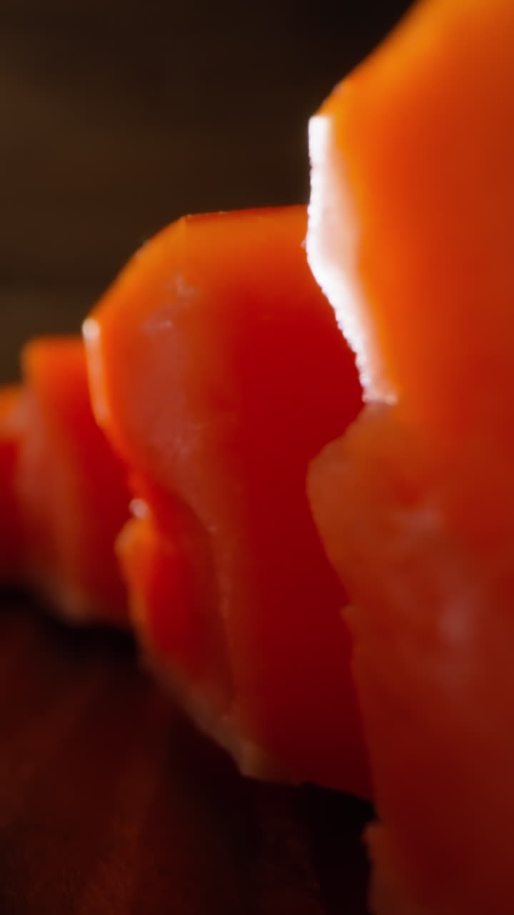 Motion between lines of tasty natural red cool smoked pink salmon cubes lying on rustic wooden table at bright light extreme closeup slow motion
