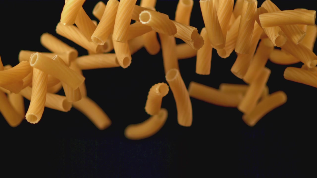 Pasta maccheroni secca che cade al rallentatore su sfondo nero.