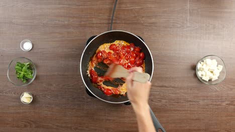 top down shot of wooden spatula stirring creamy tomato sauce in large pan on wooden table with other ingredients