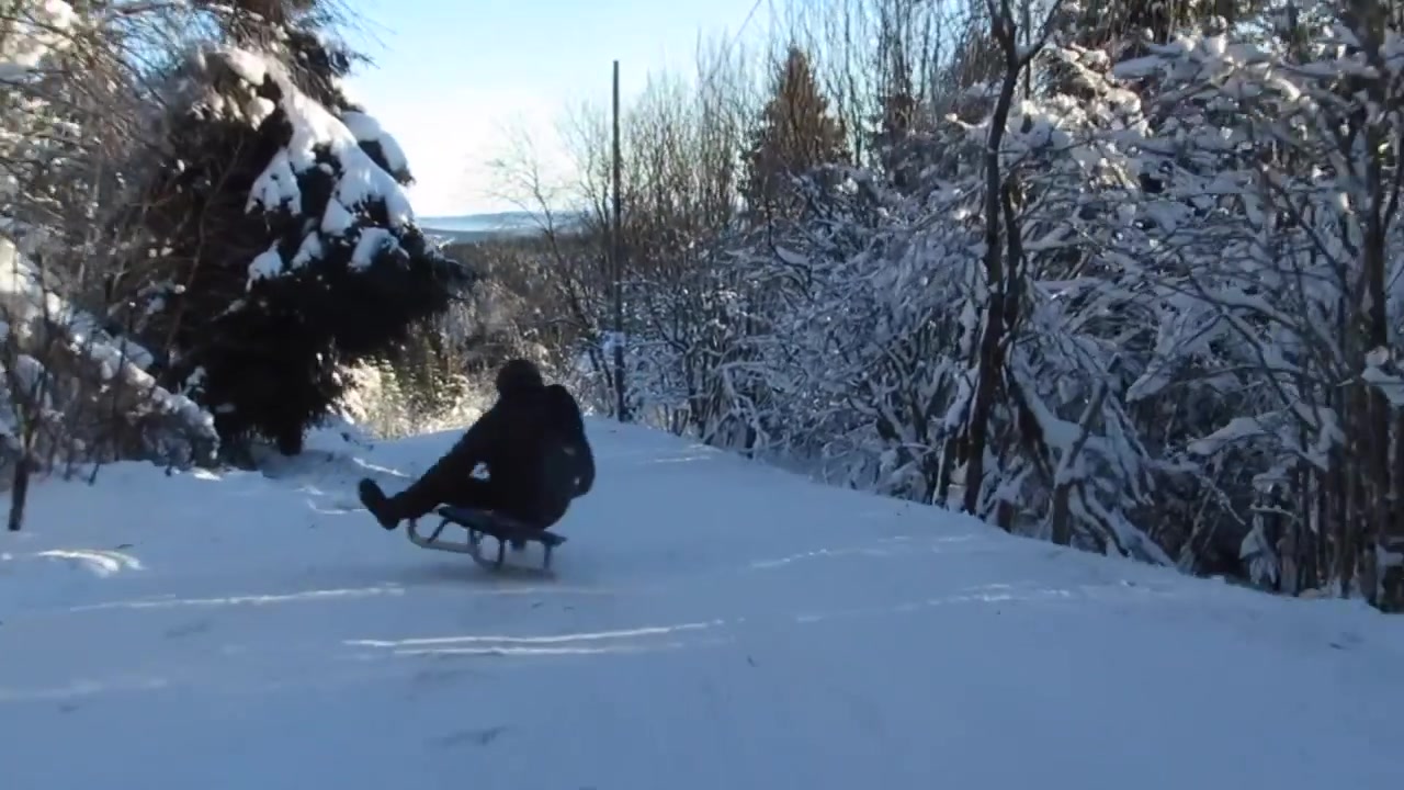 POV sledder watches other person crashing his sled on a snowy hill