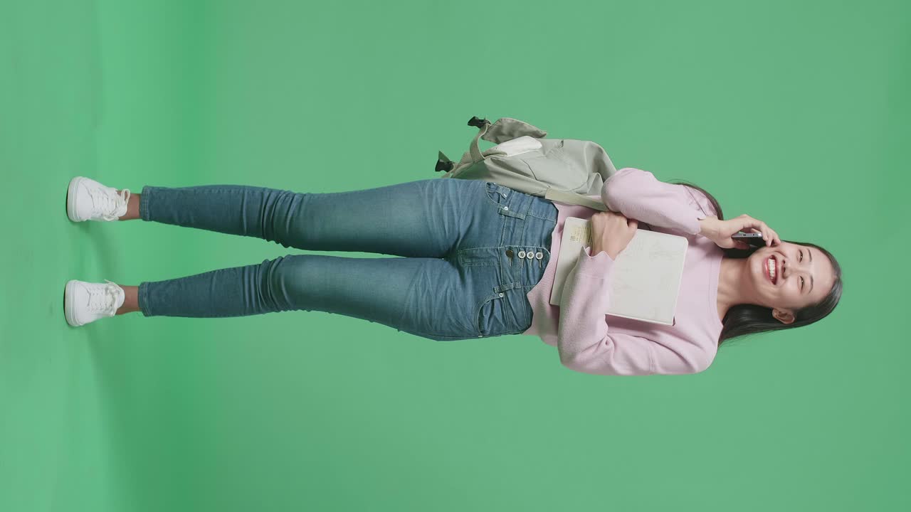 Full Body Of Asian Woman Student Talking On Mobile Phone In Green Screen Studio