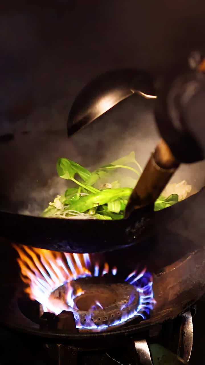 Un cuoco salta in padella noodles sukiyaki, verdure e carne in un wok con un'illuminazione drammatica.