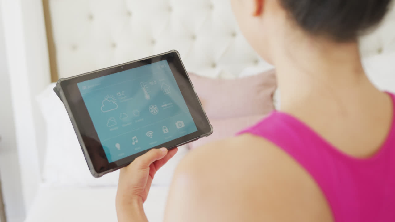 침실에서 슬로모션으로 스마트 홈 인터페이스를 가진 태블릿을 사용하는 아시아 여성