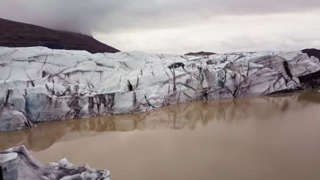 Low-flyover-aerial-of-glacier-tongue-in-Iceland,-textured-black-and-white-patterns-in-ice