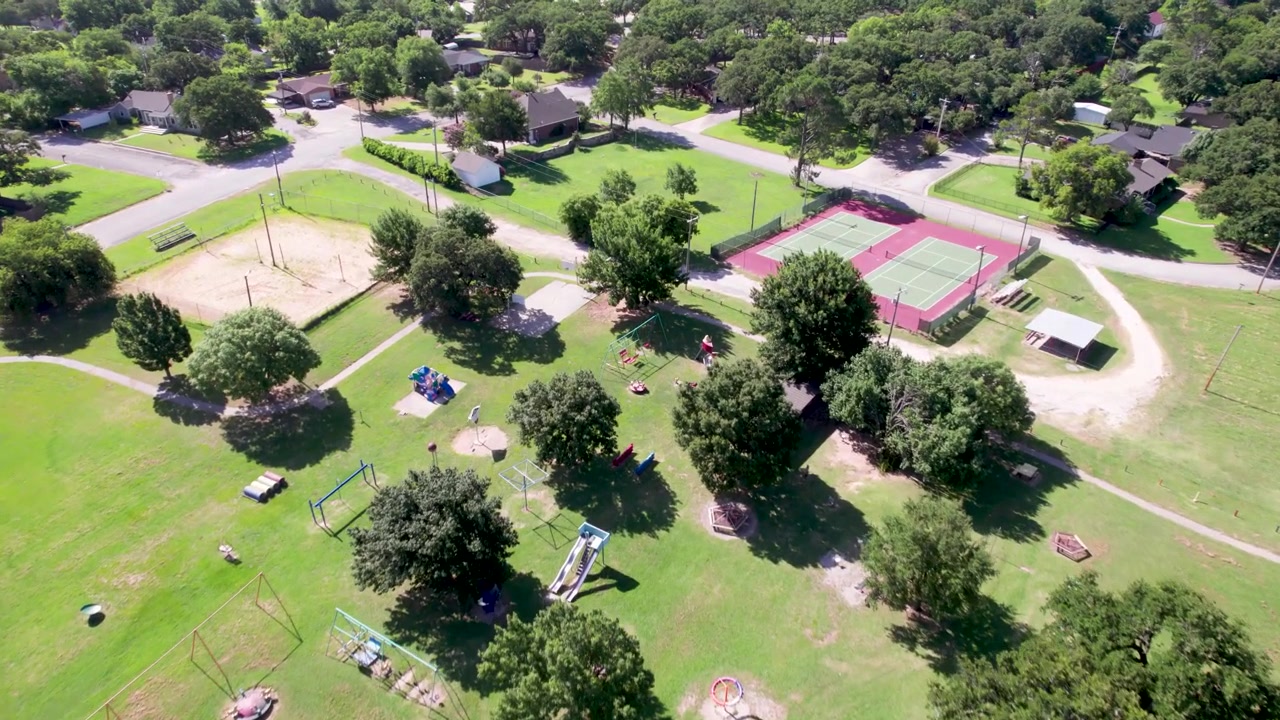 Aerial video of Enid Justin Park in Nocona, Texas. Camera flies fast over the playground equipment and tennis courts.