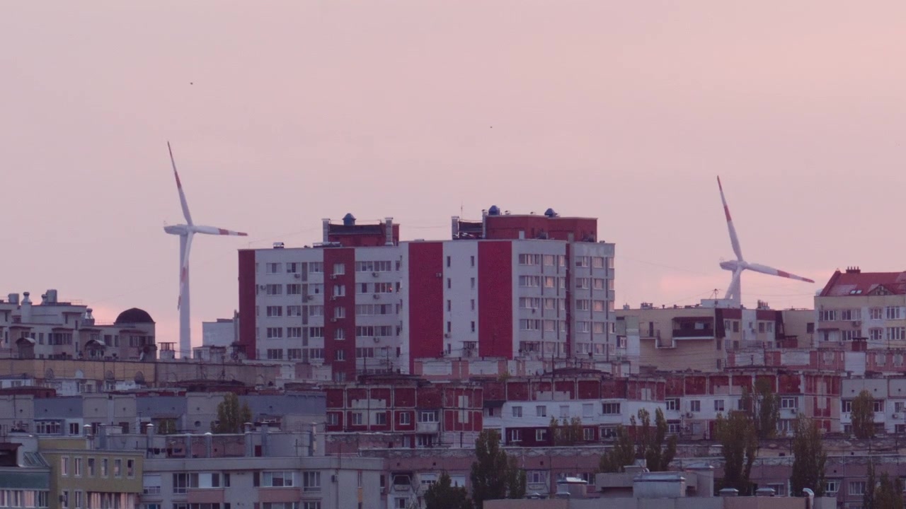 Turbinas eólicas girando atrás de edifícios residenciais ao pôr do sol