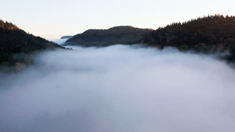 high aerial pan left above fog in misty mountain valley at sunrise