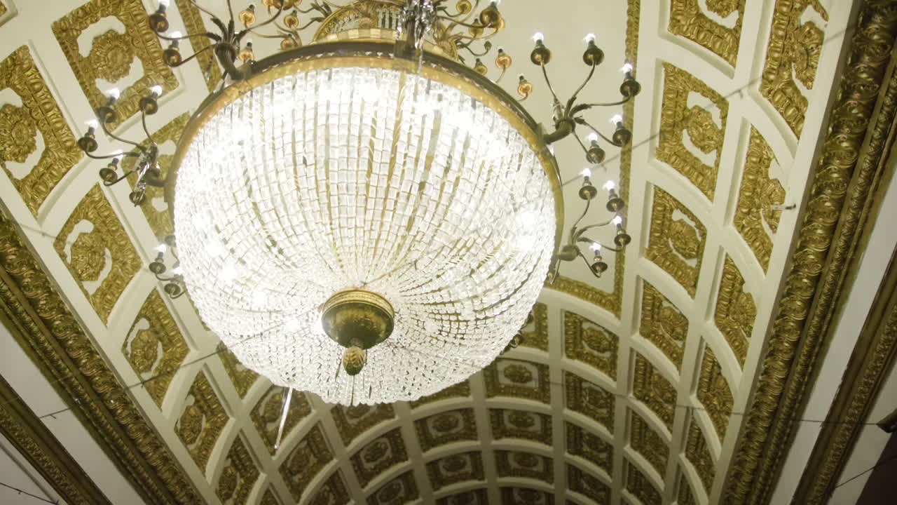 Lampadario di cristallo sotto un soffitto dorato e ornato in una sala da ballo storica, con fili di cristallo scintillanti e ottone