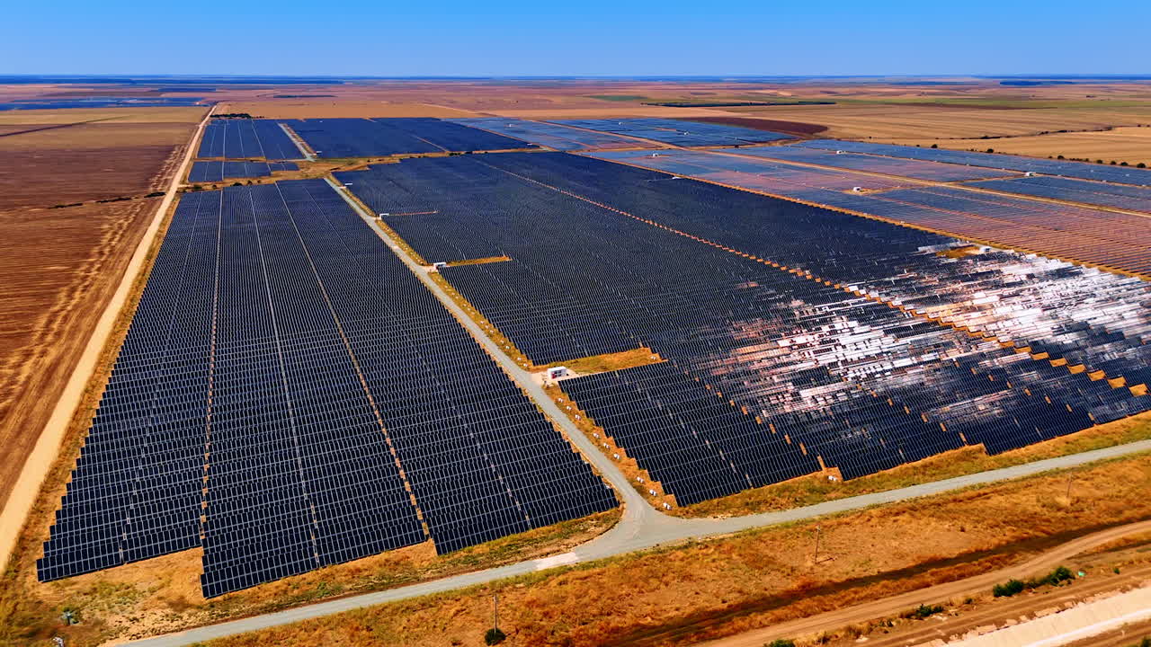 Vast solar panel field in open landscape. Rows of solar panels stretch across a flat terrain under a clear blue sky, showcasing renewable energy sources