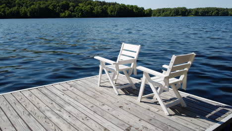 two white chairs on a wooden dock by a lake