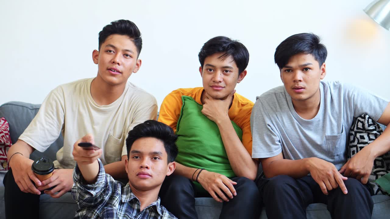 Group Of Young Asian Males Watching Comedy On TV And Laughing Heartily While Relaxing On Sofa