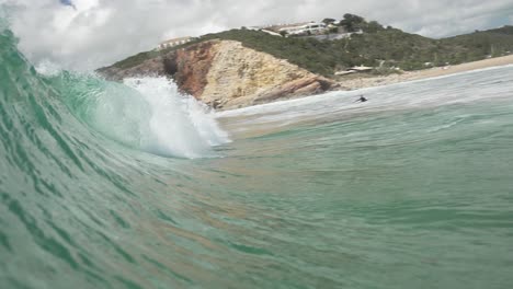 Wave-of-turquoise-water-crashing-onto-a-beach-in-an-idyllic-bay-popular-with-surfers,-underneath-a-blue-sky