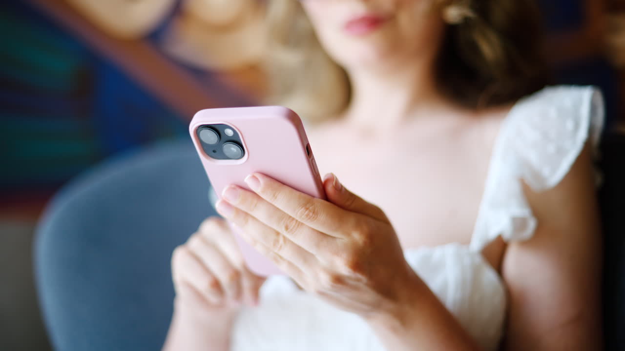 Brunette woman in white dress scrolling on her phone at a cafe