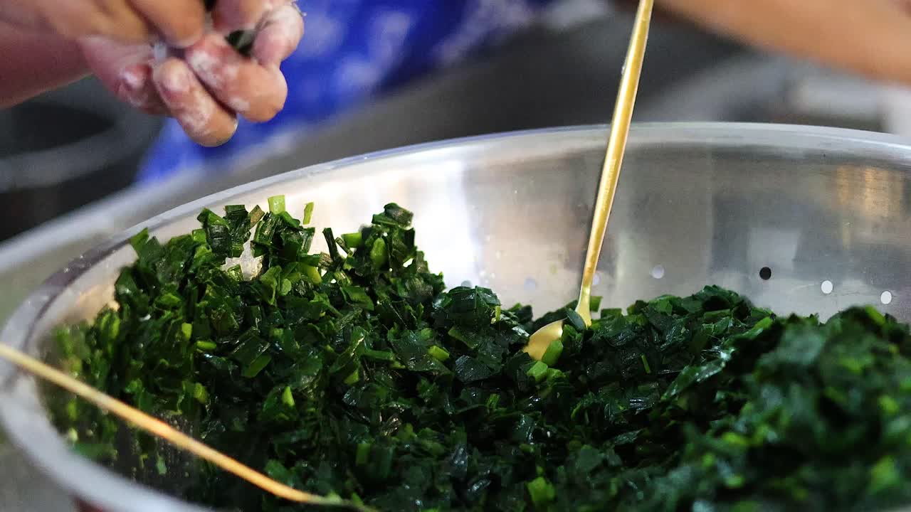 Hands making dumplings with green leafy filling