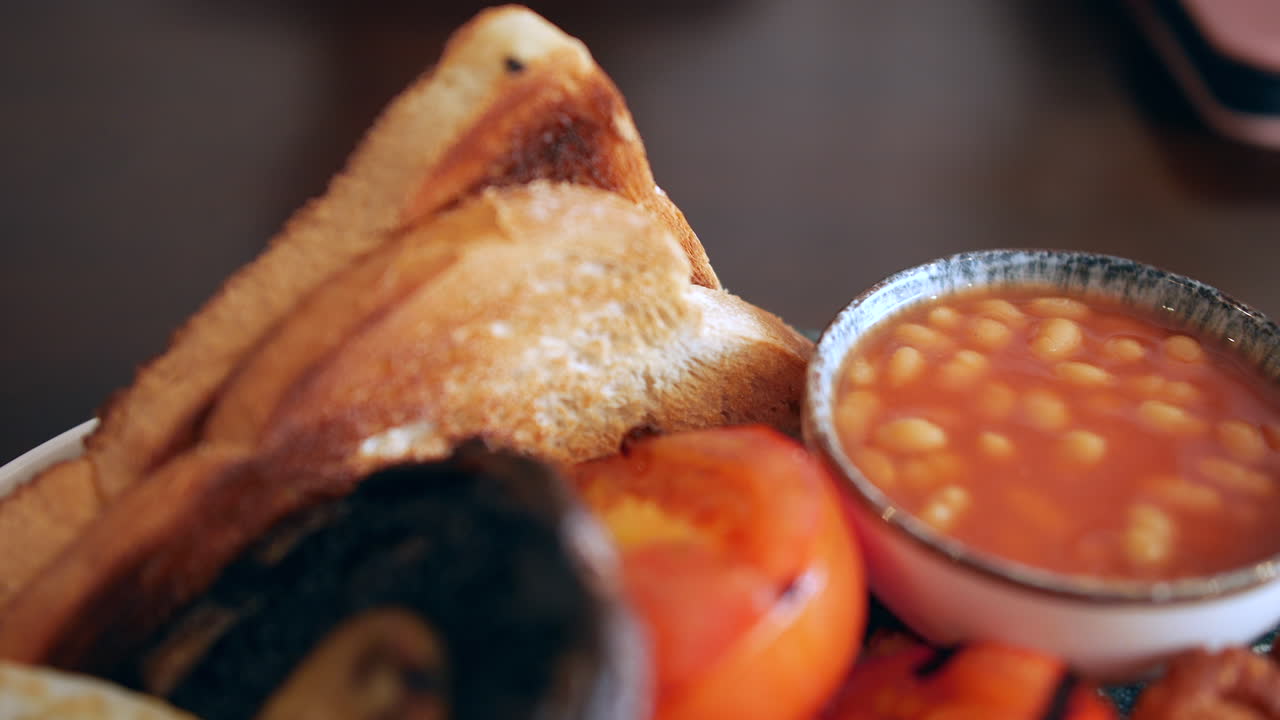A traditional English breakfast served with baked beans, toast, fried egg, grilled tomatoes, hash browns, and mushroom arranged on a plate in Padstow, UK