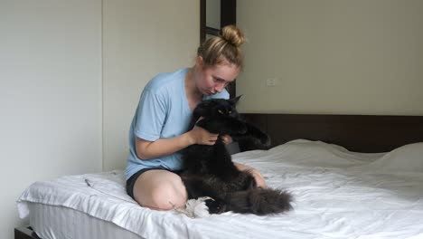 Young-woman-enjoying-bouncing-and-playing-with-her-black-pet-cat-on-bed
