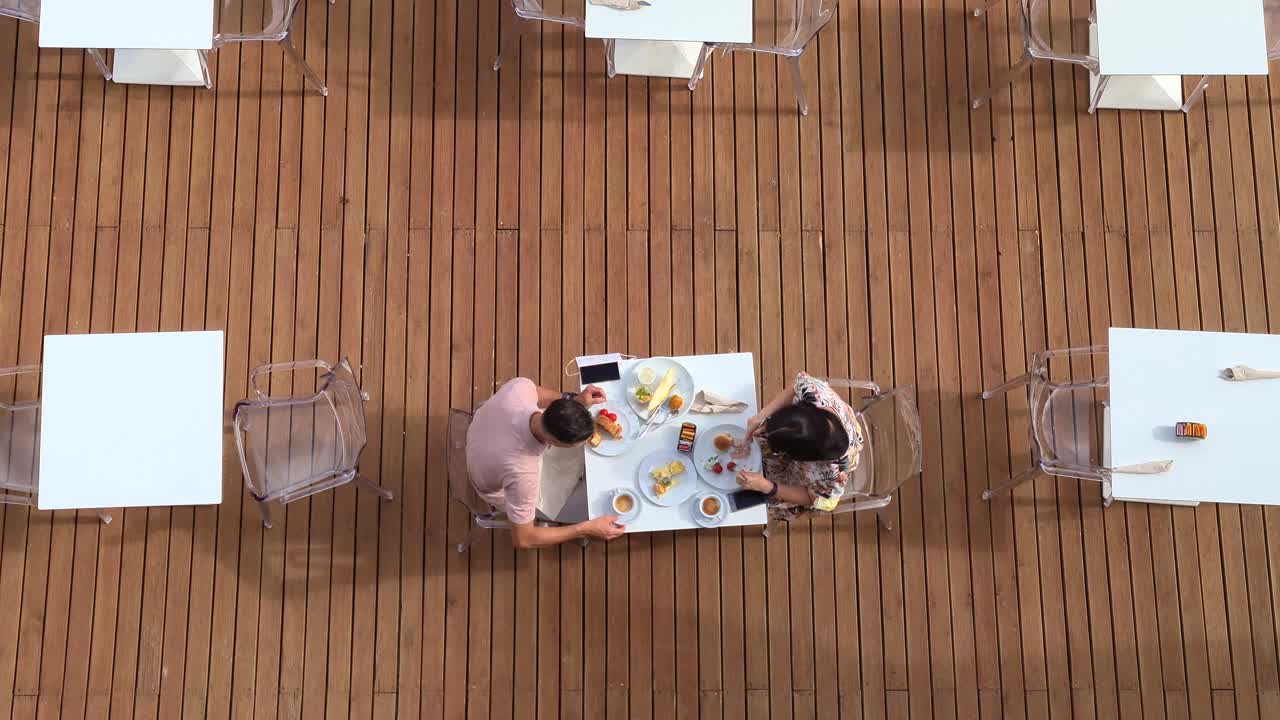 la pareja disfruta de la mañana de verano comiendo y bebiendo el desayuno al aire libre en el restaurante del hotel con una camarera sirviendo en la mesa