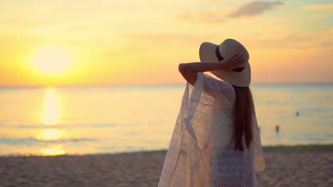 una joven asiática está sola en una playa desierta viendo cómo el cielo se vuelve rosa y dorado a medida que se pone el sol